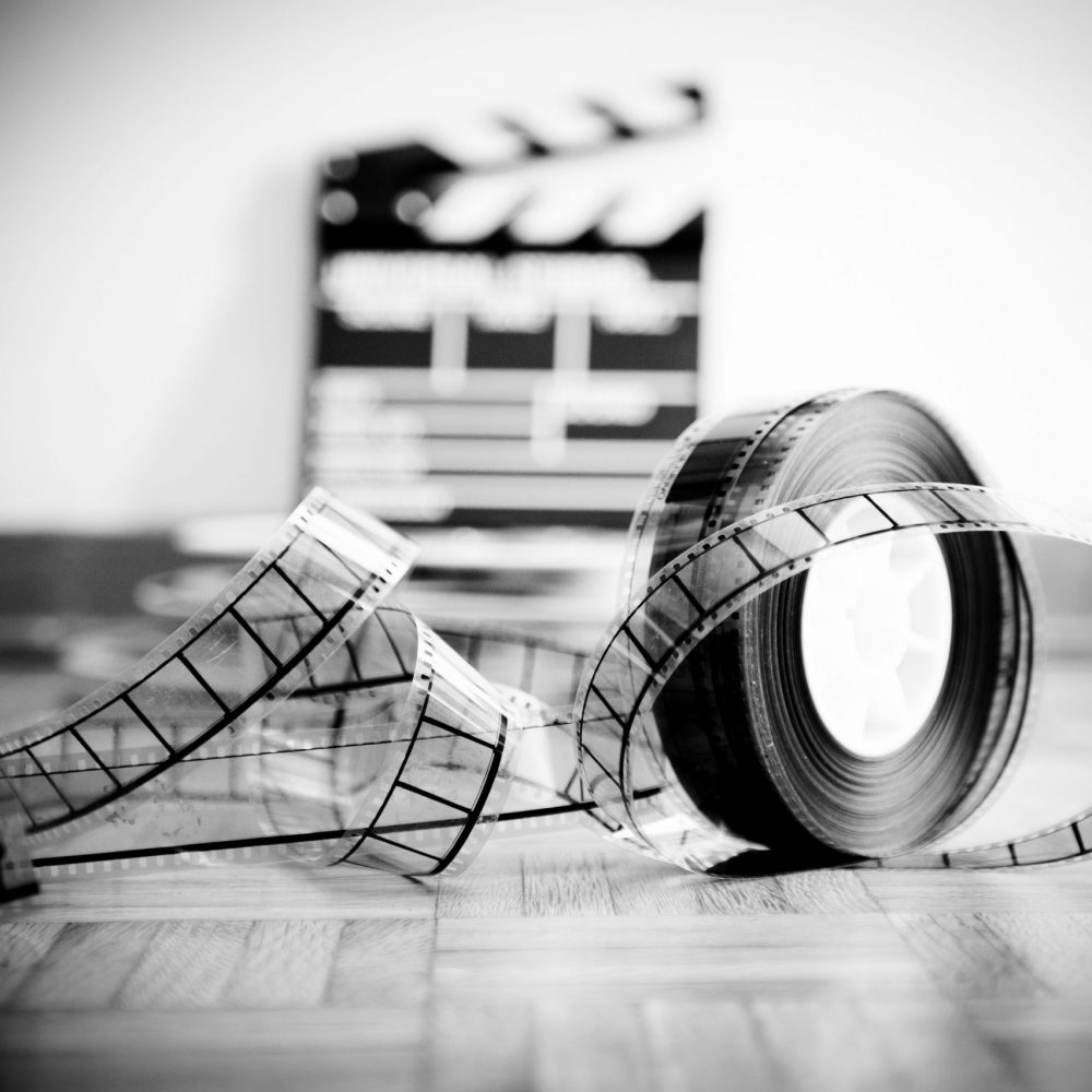35 mm cinema film reel and out of focus movie clapper board in background on wooden floor in vintage black and white